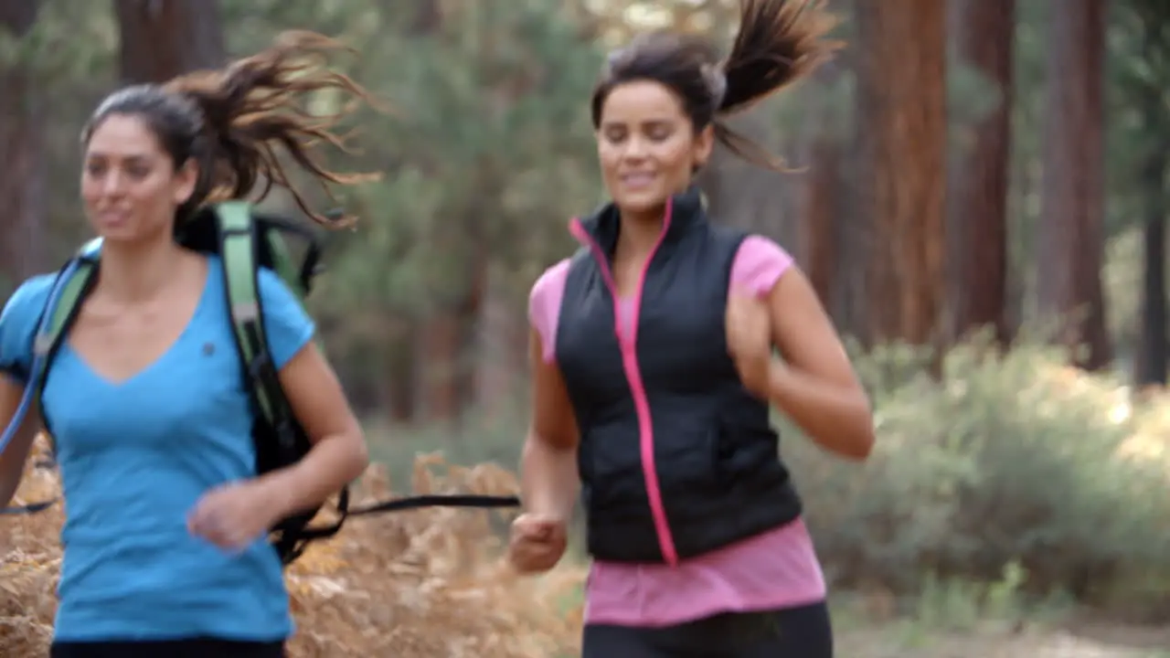 Two young women running in a forest close up