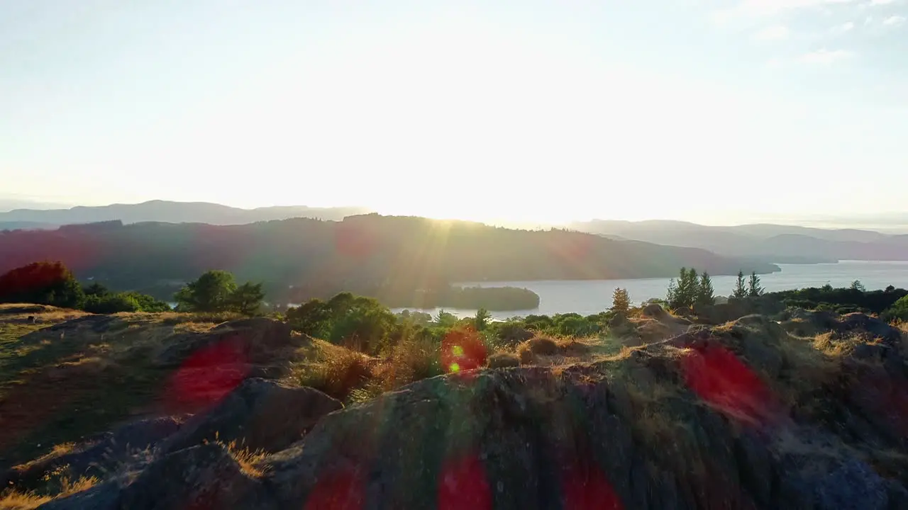 Drone shot of rolling green hills trees and Lake Windermere in sunlight with lens flare Lake District UK