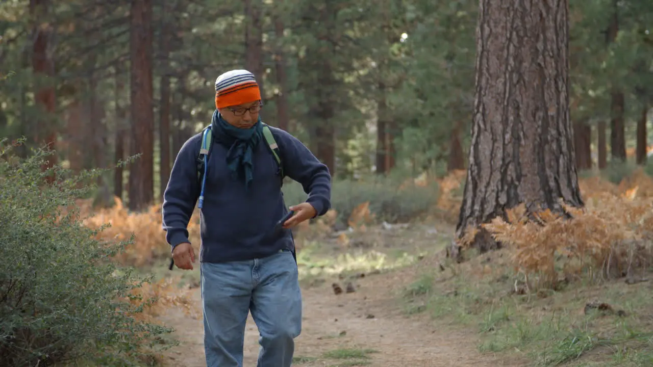 Asian man using his smartphone in a forest front view