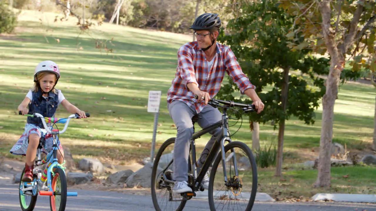 Father and daughter riding bikes on a path in a park