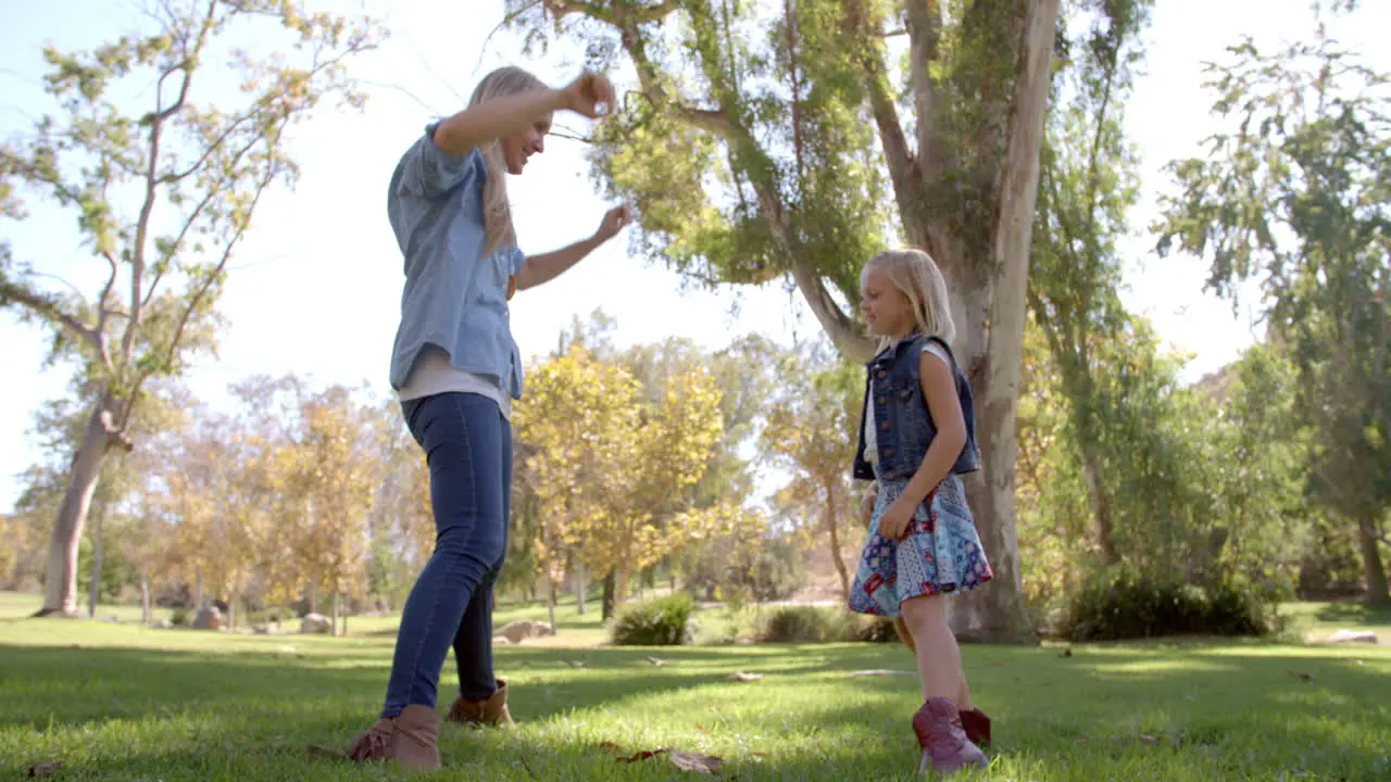 Mother and young daughter playing in a park full length