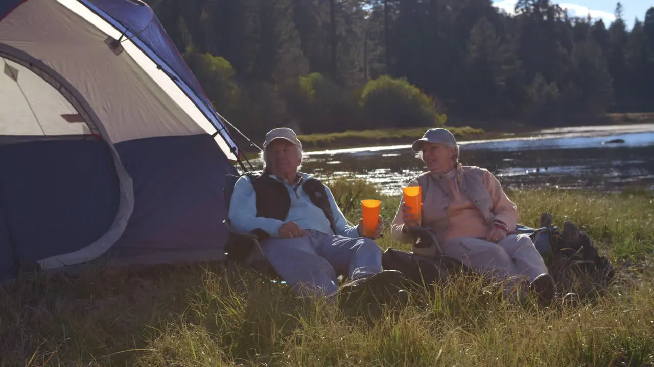 Senior couple sitting outside tent near lake closer-in shot