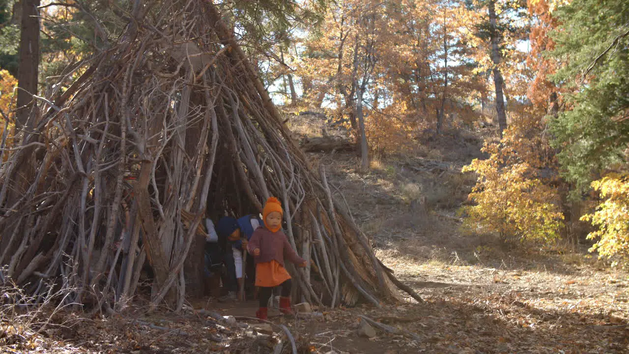 Five young children playing together leave a hut in a forest