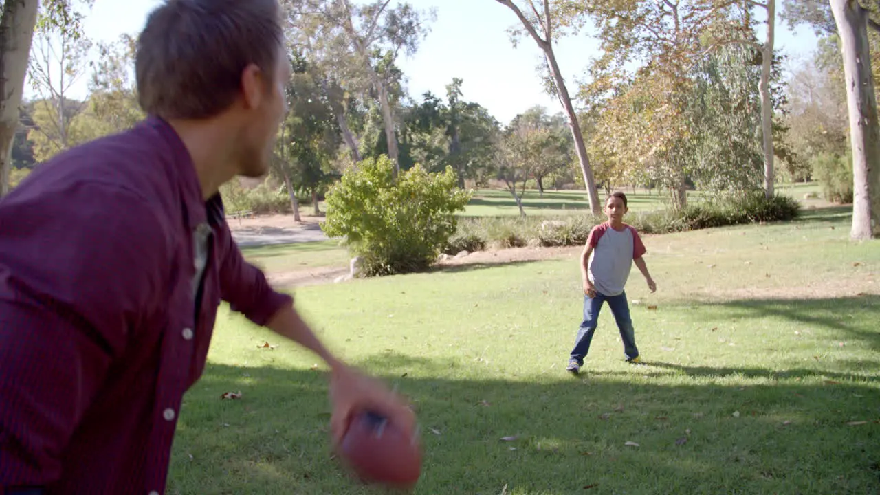 Seven year old boy throwing football with his dad in park