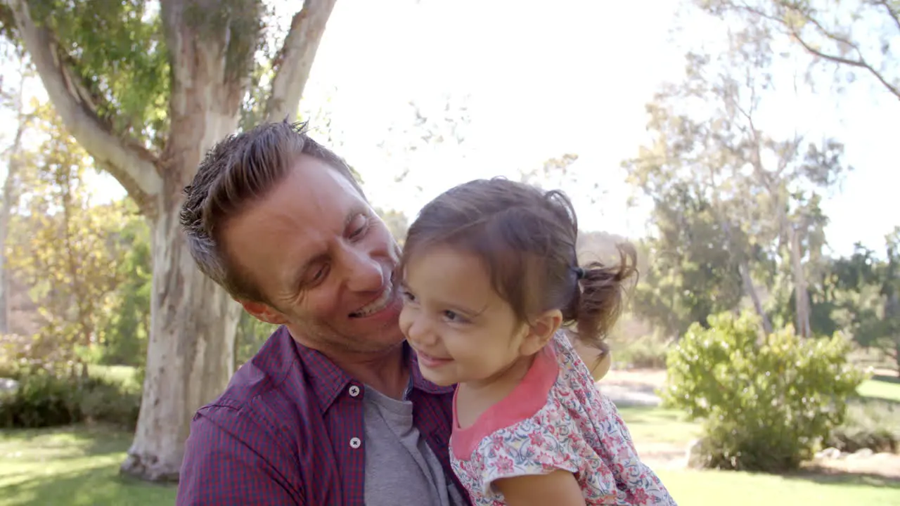 Dad holding toddler daughter in his arms at the park