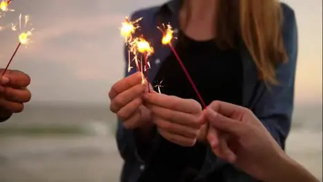 Close Up view of young people holding bengal lights during evening standing by the sea during sunset Slow Motion shot