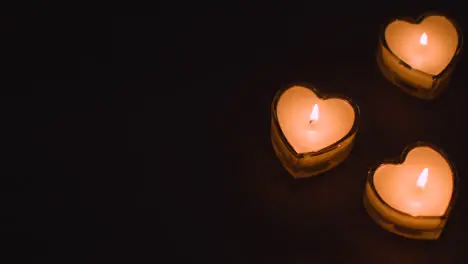 Close Up Of Three Romantic Lit Heart Shaped White Candles On Black Background With Copy Space