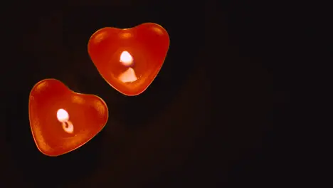 Close Up Of Two Romantic Lit Heart Shaped Red Candles On Black Background With Copy Space 2