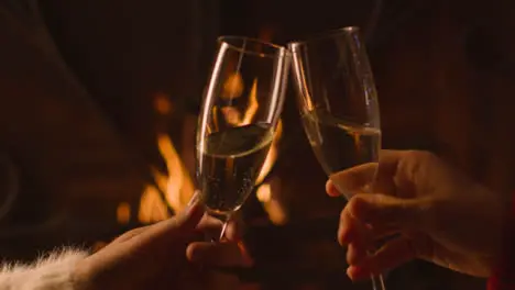 Close Up of Two People Bringing Their Champagne Glasses Together In Front of Burning Fire 