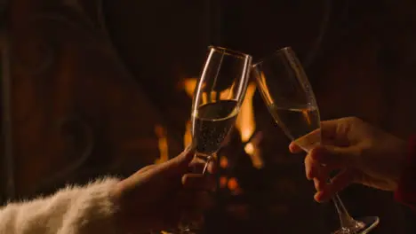 Close Up of Two People Bringing Their Champagne Glasses Together In Front of Fire 