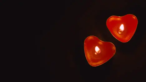 Close Up Of Two Romantic Lit Heart Shaped Red Candles On Black Background With Copy Space