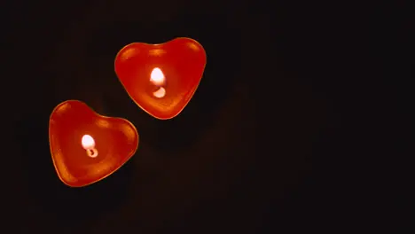 Close Up Of Two Romantic Lit Heart Shaped Red Candles On Black Background With Copy Space 1