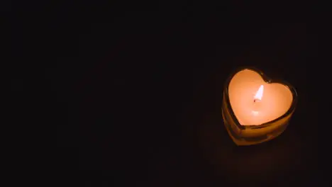 Close Up Of Romantic Lit Heart Shaped White Candle On Black Background With Copy Space