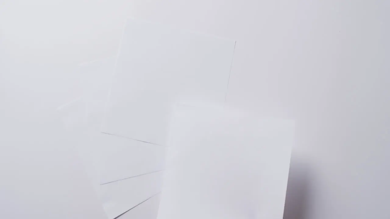 Hand holding piece of paper over pieces of paper with copy space on white background in slow motion