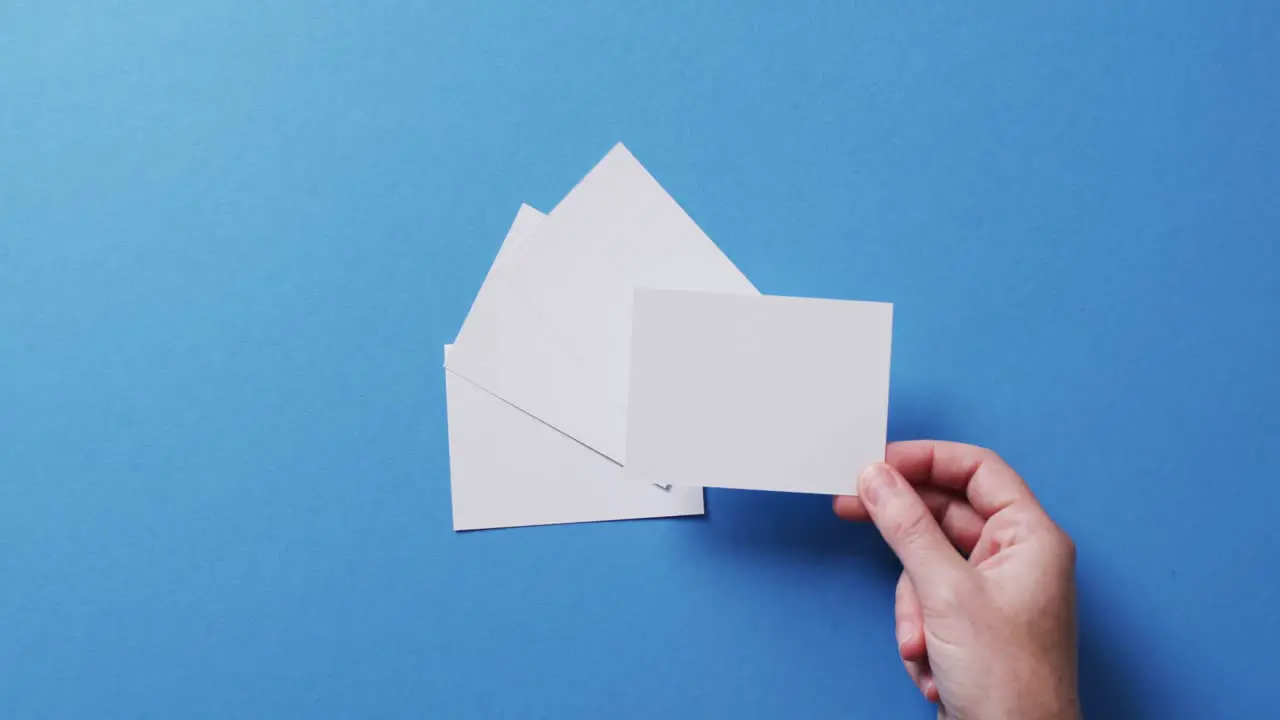 Hand holding piece of paper over pieces of paper with copy space on blue background in slow motion