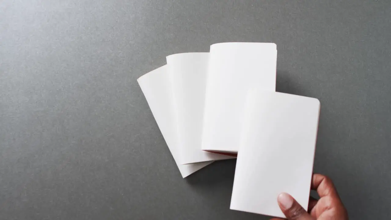 Hand holding piece of paper over pieces of paper with copy space on gray background in slow motion