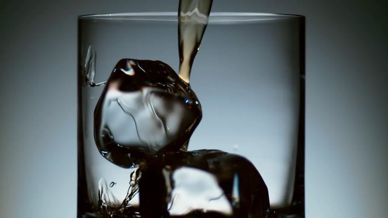 Alcohol Pouring Over Ice in Elegant Cocktail Glass