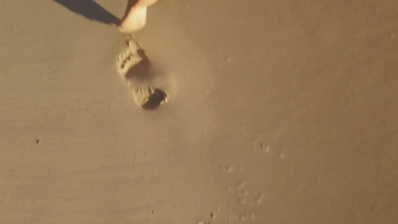 A slow motion shot of woman´s feet leaving footprints on the sand just in the shore