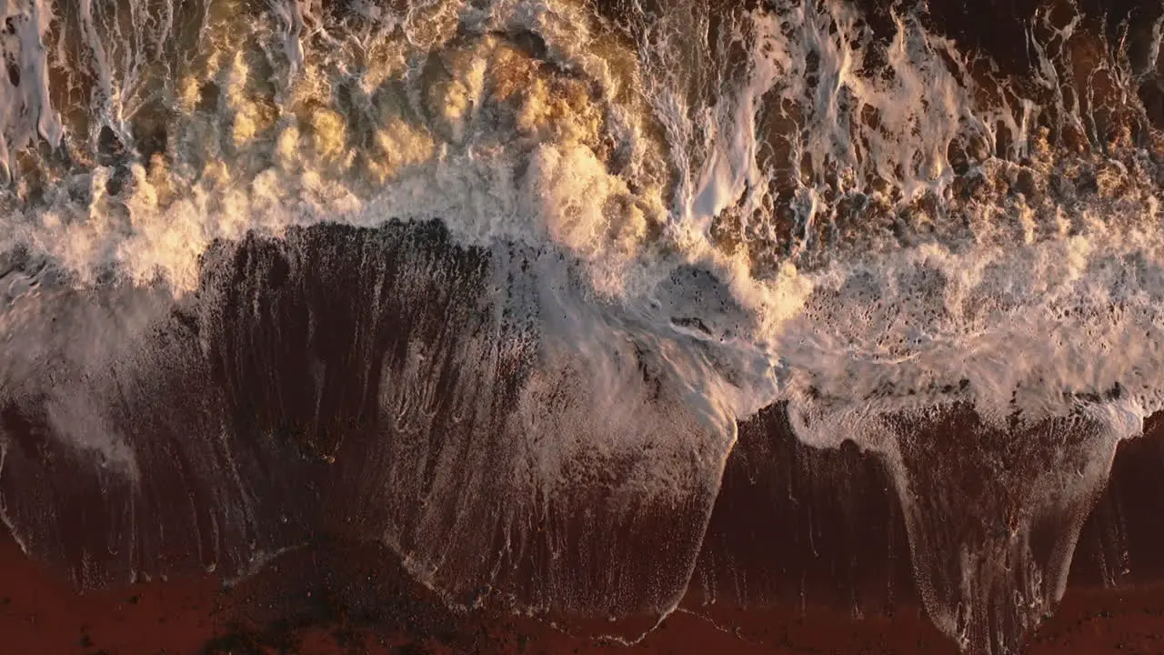 Slow motion aerial view of waves crashing into a beach at sunset