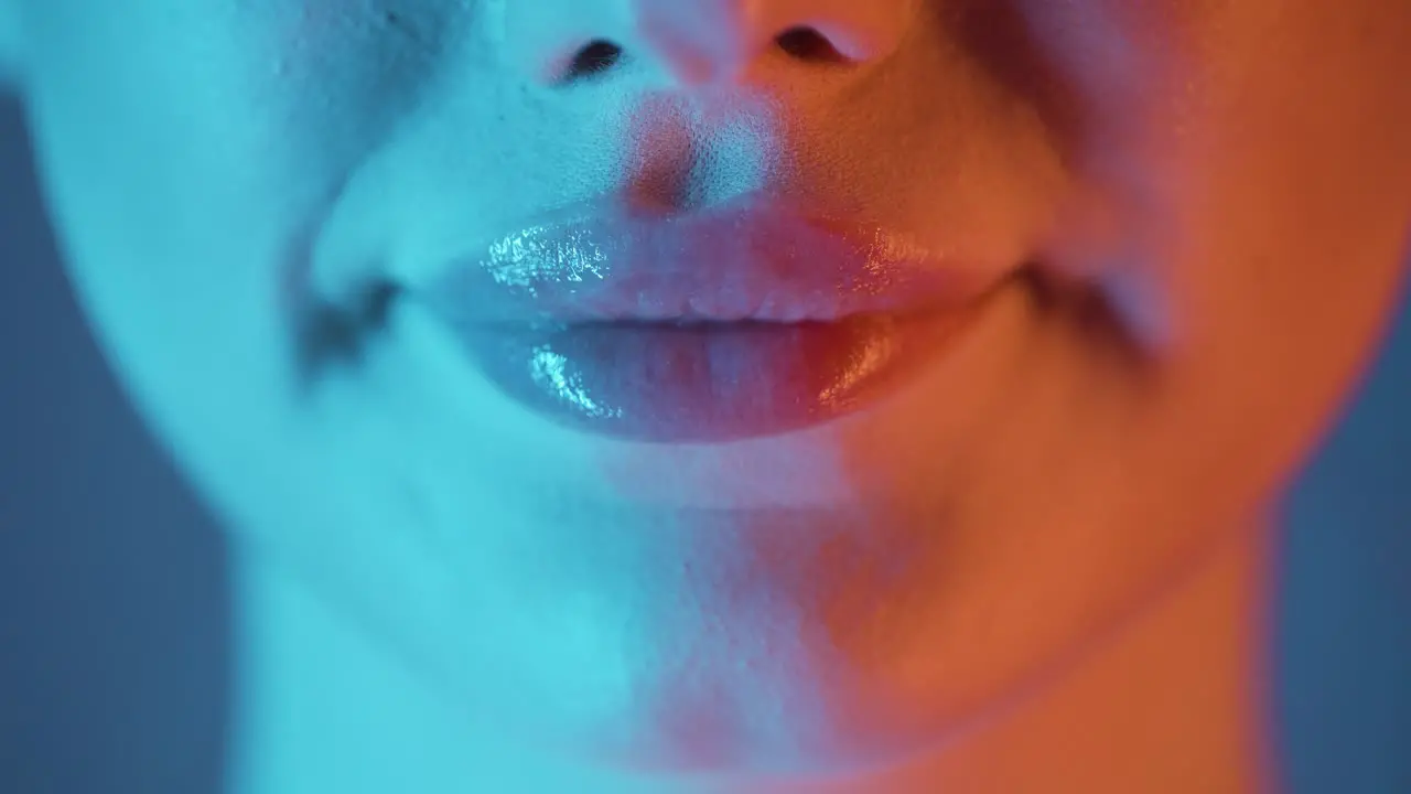 Extreme close up of beautiful full woman lips with applied lip gloss while the woman symbolizes a gesture of joy with orange blue contrast in her face in slow motion