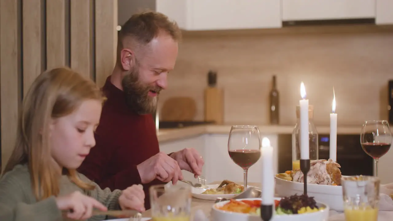 Camera Focuses A Father And Daughter Having Dinner At Christmas Sitting At The Table And Talking With Other Family Members