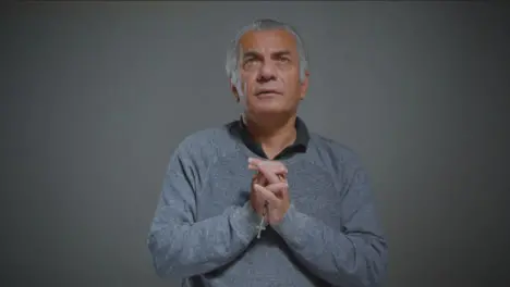 Portrait Shot of Senior Man Praying with Rosary Beads