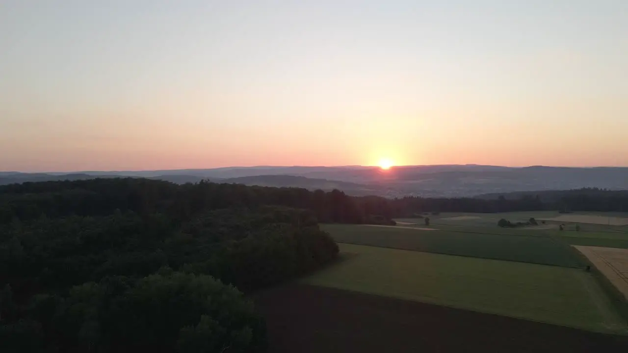 Static drone footage at sunset of meadows and corn fields in a valley surrounded by forests in germany