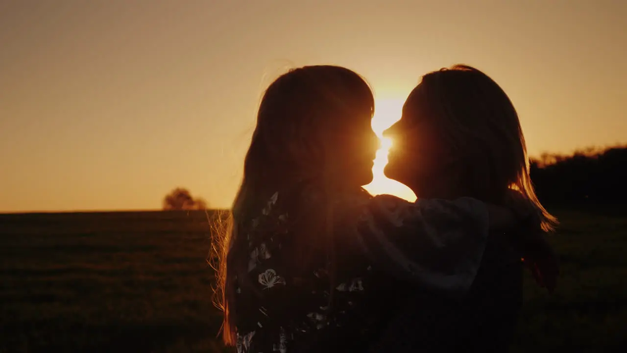 A Woman Kisses Her Daughter Tenderly The Sun At Sunset Beautifully Illuminates Their Silhouettes 4K 