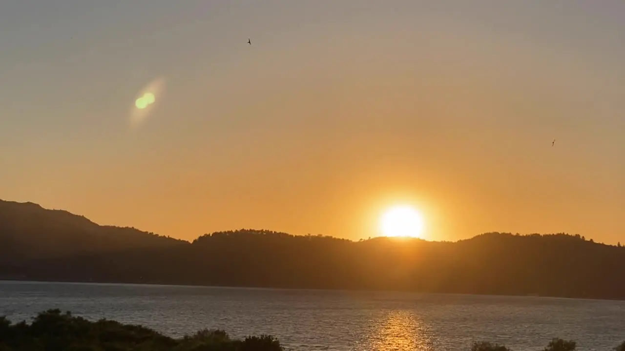 Zoom out of sun setting behind silhouetted ridge