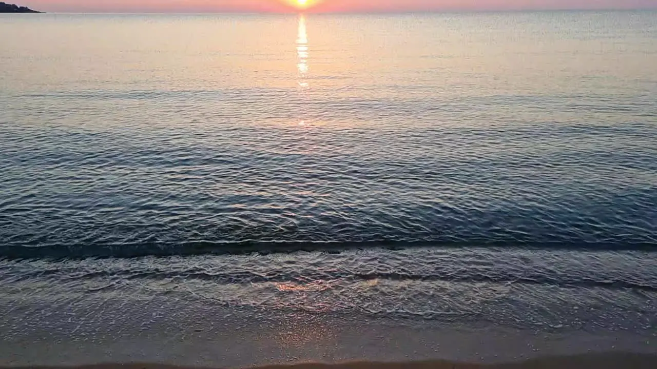 Calm water surface and sea waves splashing on sandy beach at sunrise