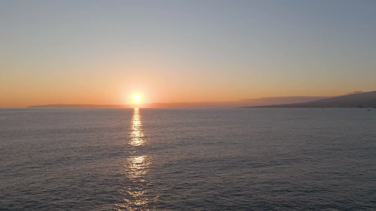 Cinematic aerial sunrise reflection over ocean with Pico Island on horizon