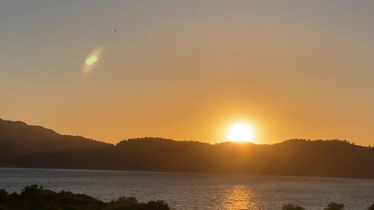 Lens flare of sun through huge river on panorama of mountain landscape at sunrise and bright disk of sun in morning in summer against blue sky aerial view of drone forward