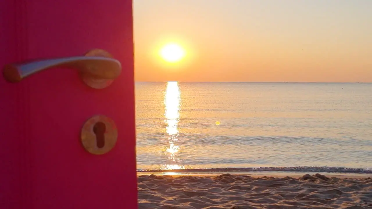 View through an open door to the ocean and sandy beach at sunrise