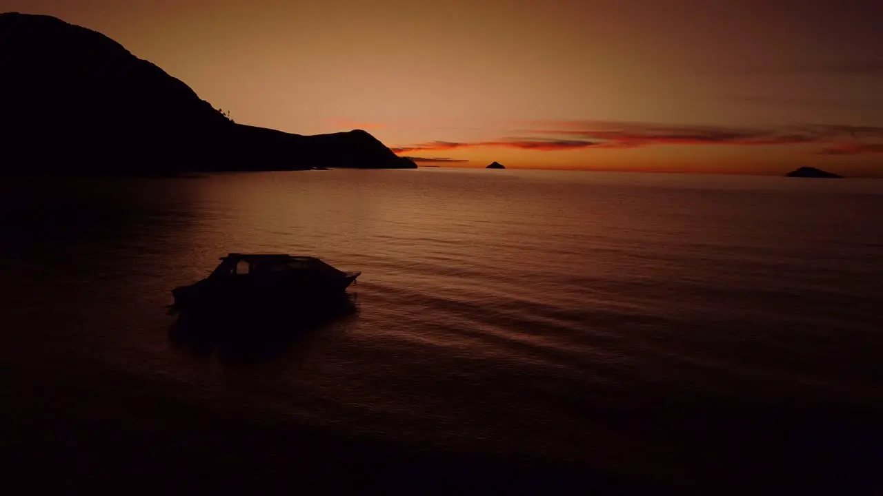 Slow aerial shot of a dark orange sunset at dusk with a boat on Lake Titicaca in Peru