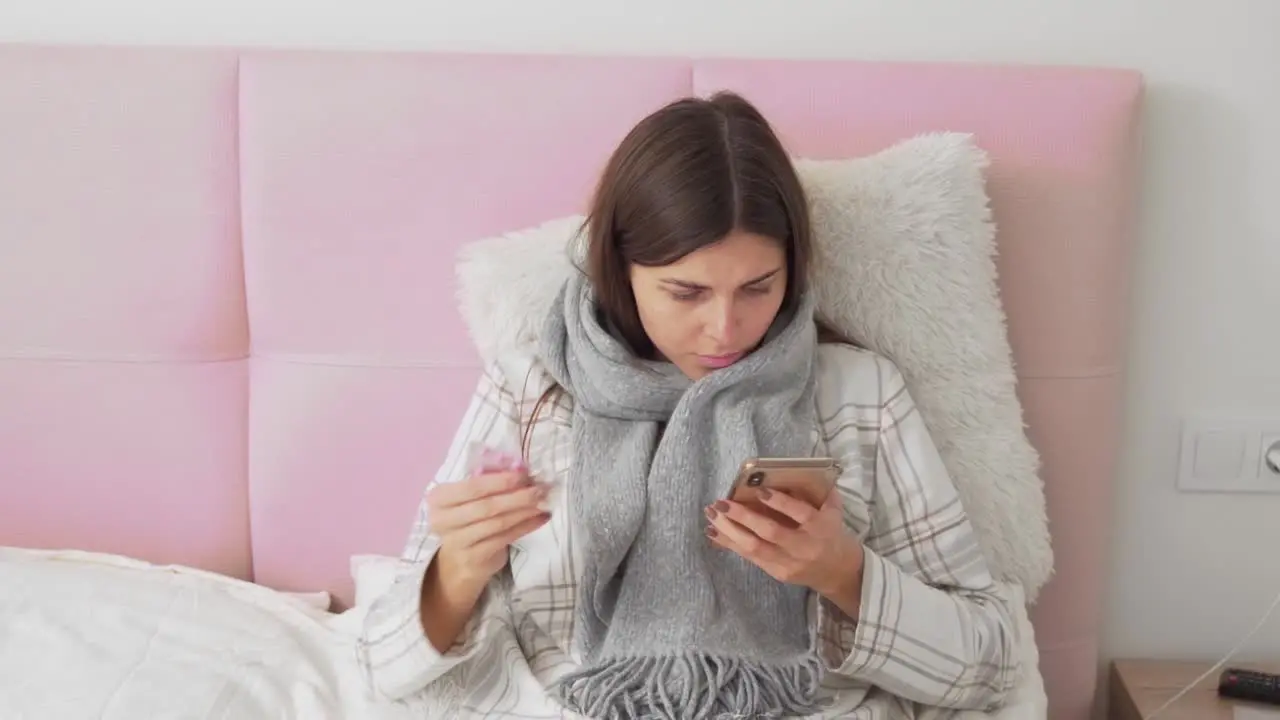 sick girl lying in bed reading on the phone about pills and drinking tea