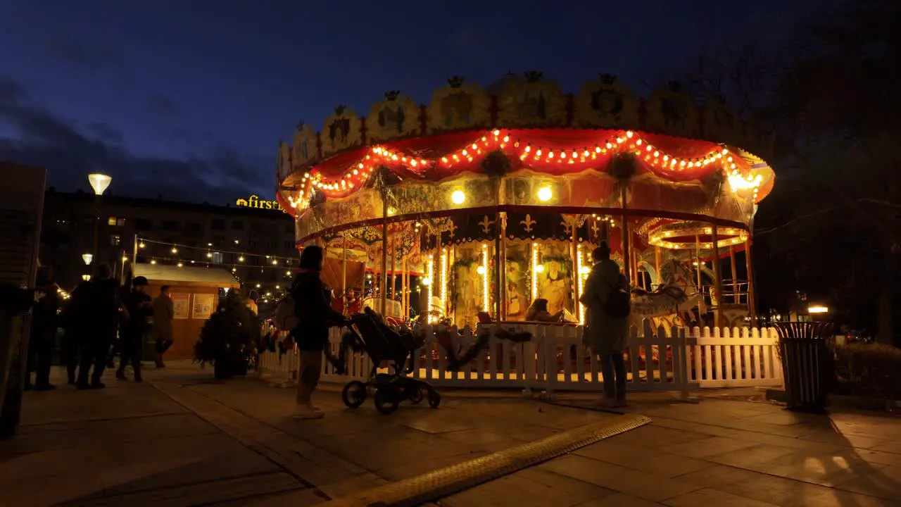 carousel or a merry-go-round spinning in the dark the kids' mothers looking at them and people walking around at the Sofia Christmas Fest 2023