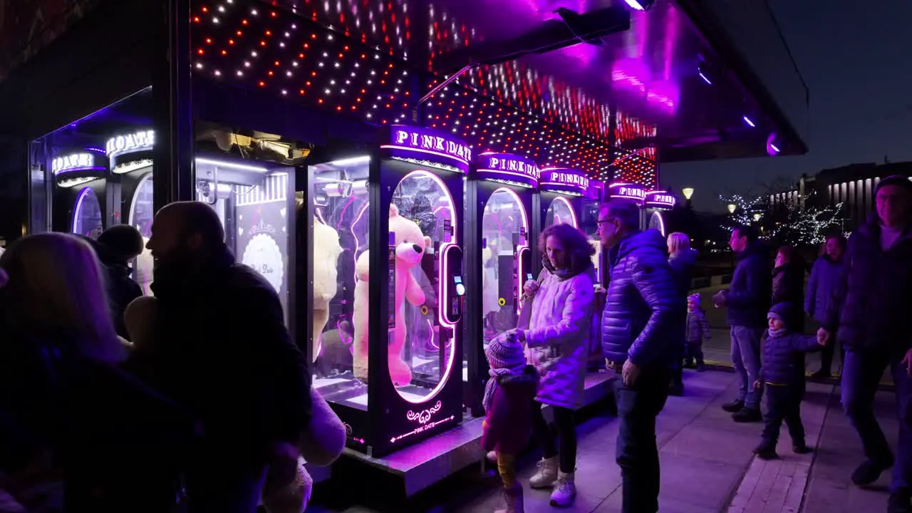 Night footage of people at PINK DATE arcade game vending machines where you have to cut the rope holding a giant teddy bear to win it