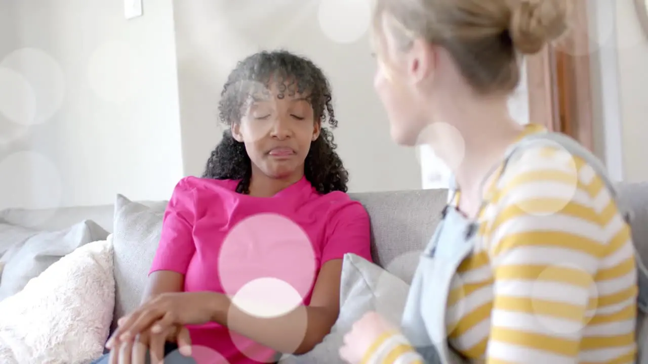 Animation of light spots over two diverse teenage girls talking on couch