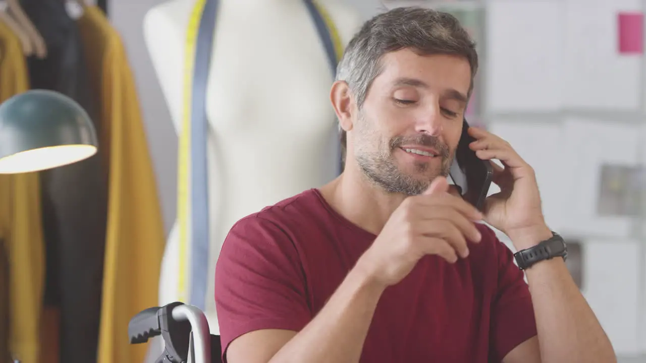 Mature Male Fashion Designer In Wheelchair In Studio Talking On Mobile Phone