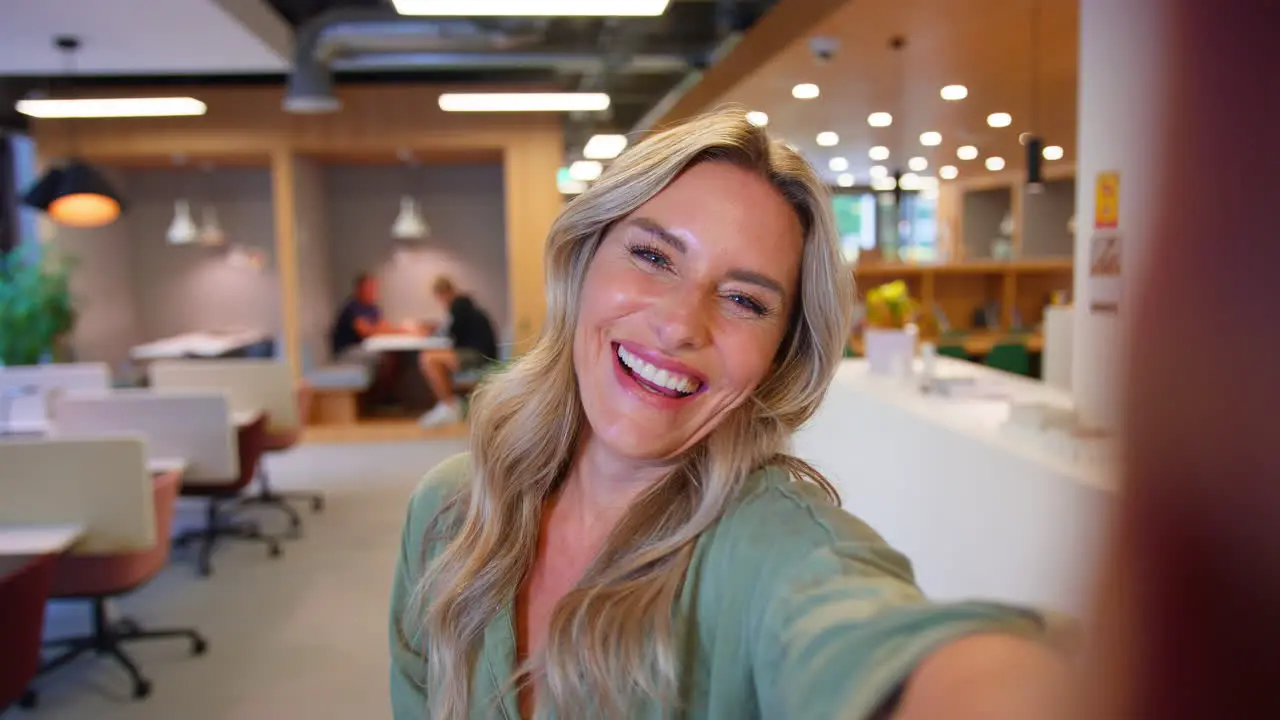 POV Selfie Portrait Of Mature Businesswoman In Modern Office Waving To Mobile Phone Camera