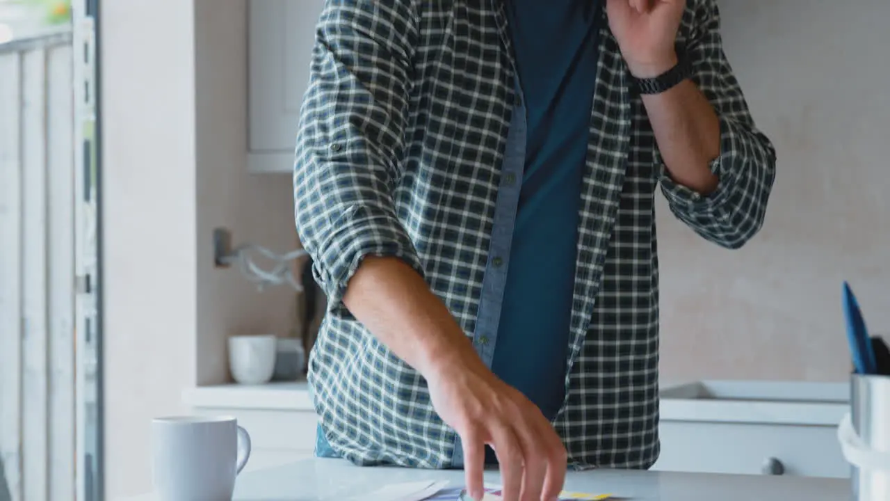 Man Renovating Kitchen At Home Looking At Paint Swatches And Talking On Mobile Phone