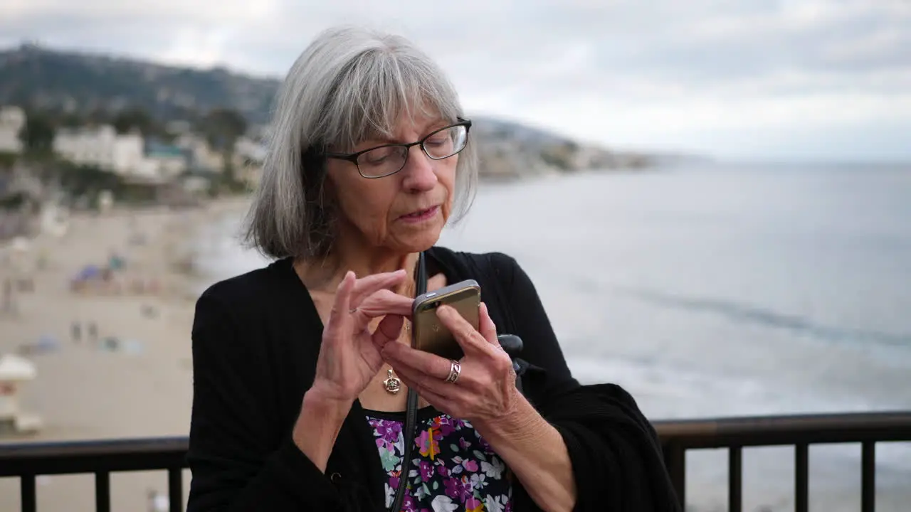 A middle aged woman with aging white hair and eye glasses texting on her phone on vacation in Laguna Beach California SLOW MOTION