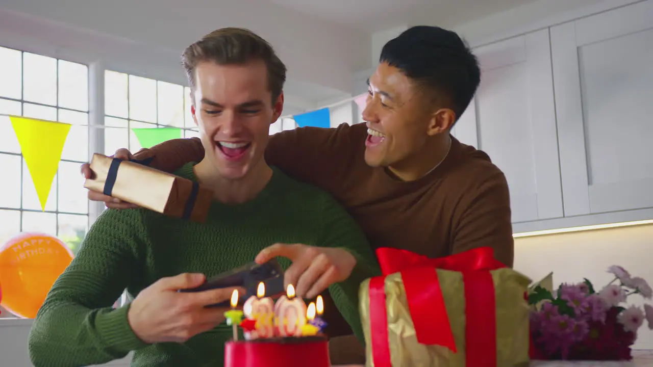 Same Sex Male Couple Celebrating 30th Birthday At Home With Man Taking Photo Of Cake On Phone