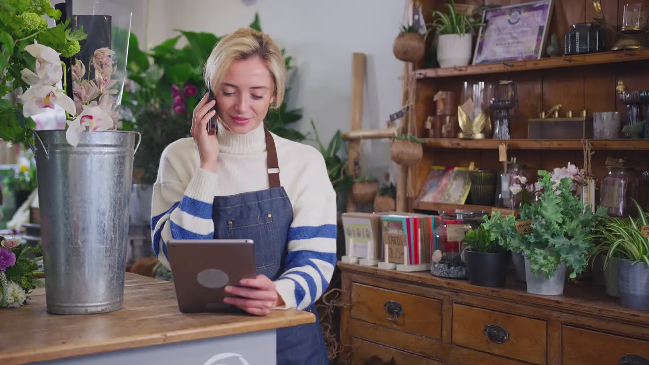 Female Owner Of Florists Shop With Digital Tablet Talking On Mobile Phone