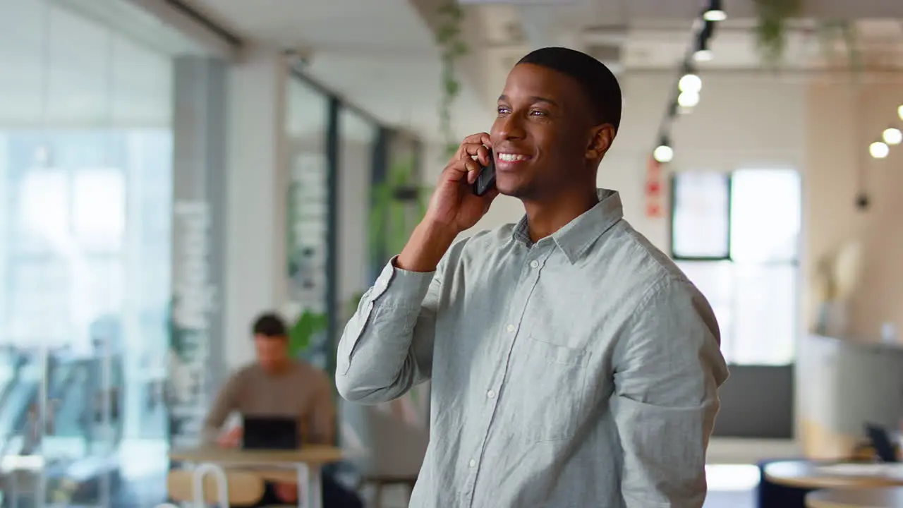 Businessman Standing In Modern Open Plan Office Talking On Mobile Phone