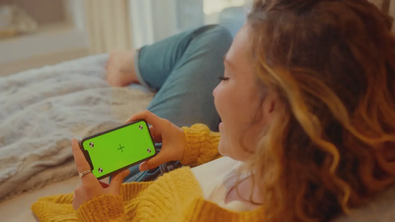 Over The Shoulder View Of Woman At Home Watching Or Streaming Film On Mobile Phone With Green Screen