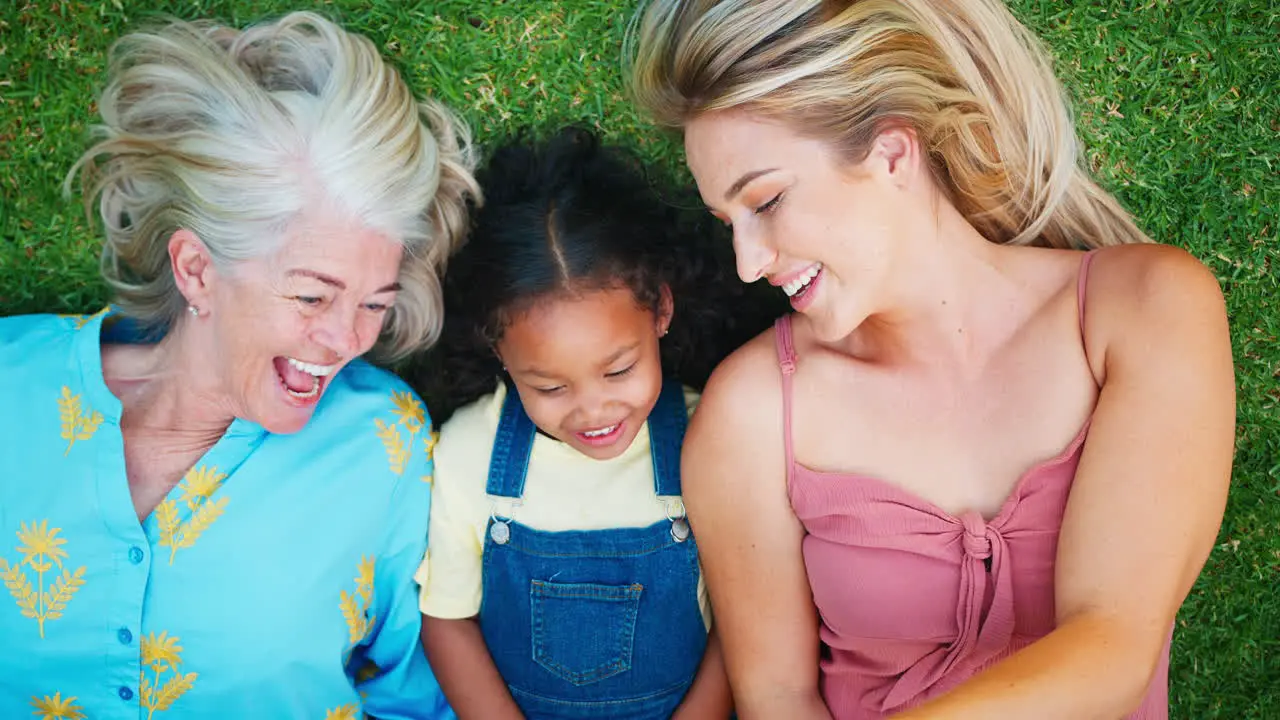 Overhead Shot Of Multi-Generation Female Family Lying On Grass Taking Selfie On Mobile Phone