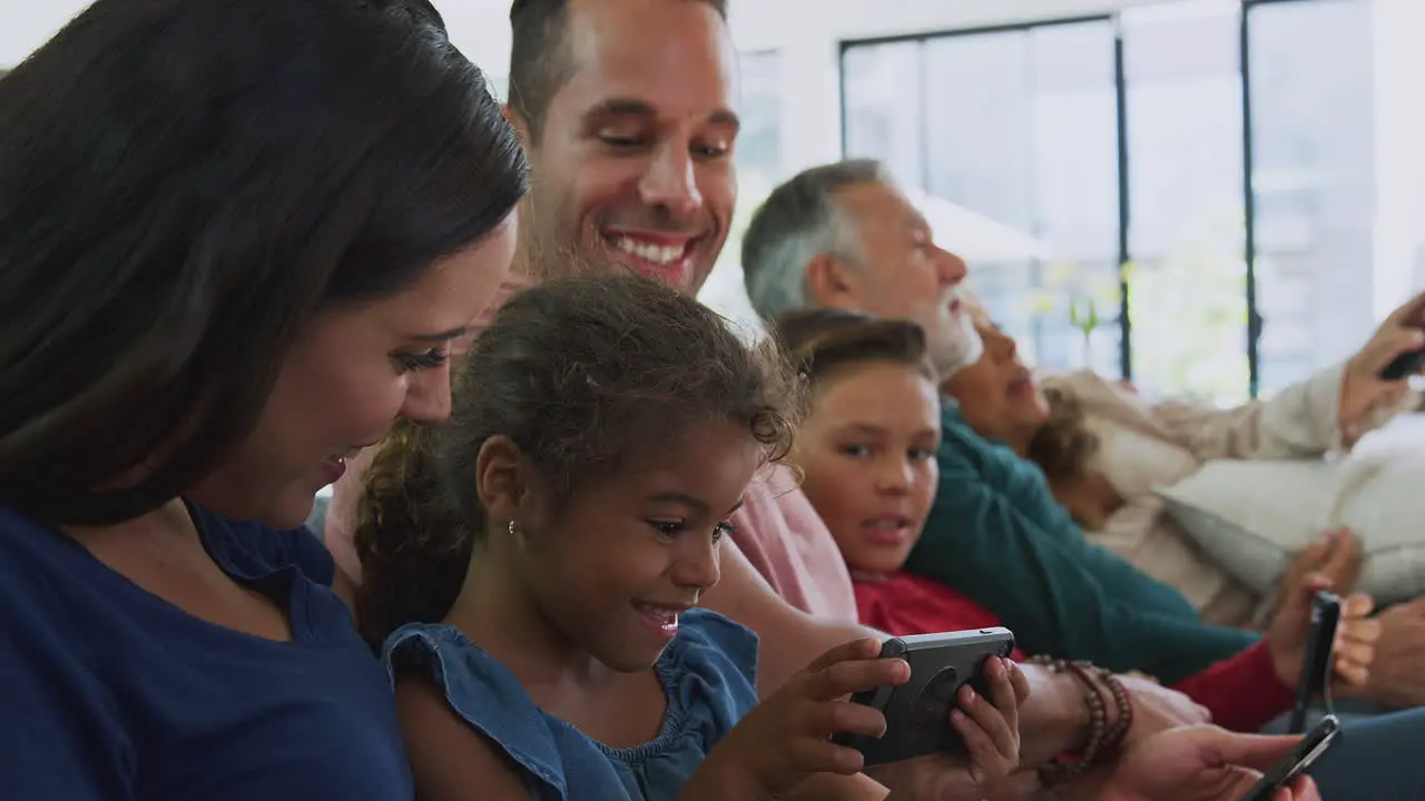 Multi-Generation Family On Sofa Watching TV And Playing With Digital Tablet And Mobile Phones