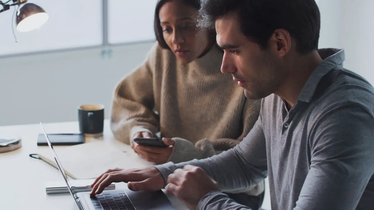 Businessman Working On Laptop At Desk Collaborating With Female Colleague Using Mobile Phone