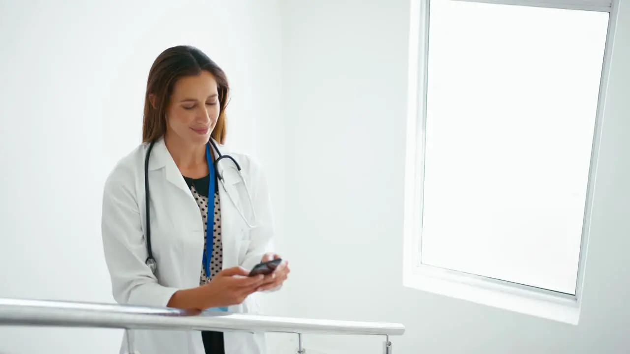 Female Doctor In White Coat Browsing On Mobile Phone On Stairs In Hospital